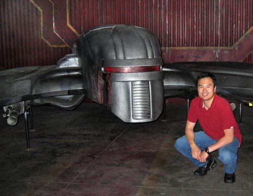 photo of Eric Chu crouching next to a model of a cylon ship