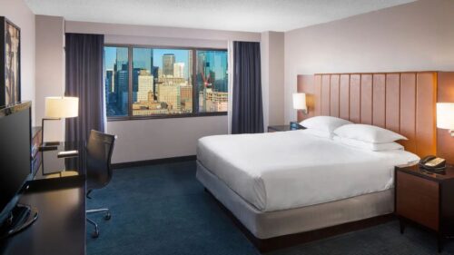 Photo of a 1 king bed room at the Hyatt Regency Minneapolis, showing a cityscape view out the window and a large bed with two lamps