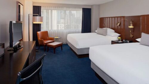 Photo of a 2 queen beds room at the Hyatt Regency Minneapolis, showing both beds next to each other, a chair, dresser with TV, and desk