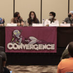 Panelists wearing face masks at a table with a CONvergence banner on it at CONvergence 2022