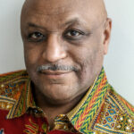 Headshot of Maurice Broaddus, an older Black man. He is bald and has a salt-and-pepper mustache. He is wearing a very colorful shirt.