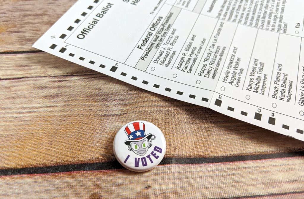 Photo of 1" pinback button showing Connie wearing an Uncle Sam hat and "I VOTED" in purple text.