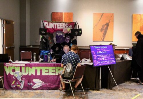 Volunteers table with volunteers staff helping someone sign up to volunteer