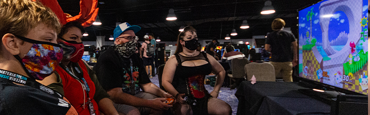 Photo of gamers playing Smash Brothers at 2d Con. They are all wearing face masks.
