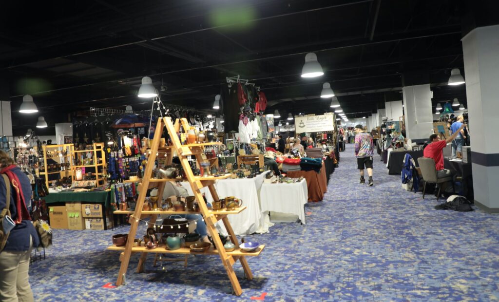 Photo of the dealers room at CONvergence 2019 showing many different booths with tons of items from shirts to pottery to toys to knick knacks
