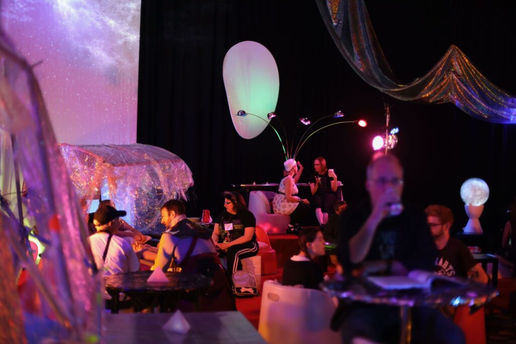 Photo of people chilling in a room flooded with purple light, sparkling backdrops, and futuristic furniture