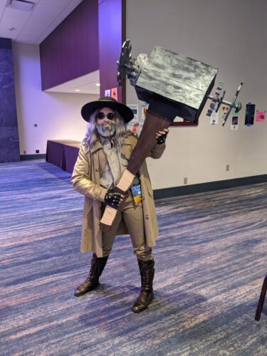 CONvergence 2021 cosplayer wearing a face mask with a gray beard on it, and carrying a gigantic hammer