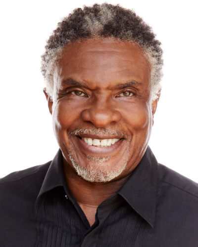 Headshot of Keith David. He is an older Black man with short white goatee-style facial hair and streaks of white hair at his temples and on the top of his short curly hair. He is smiling warmly, with twinkling eyes.