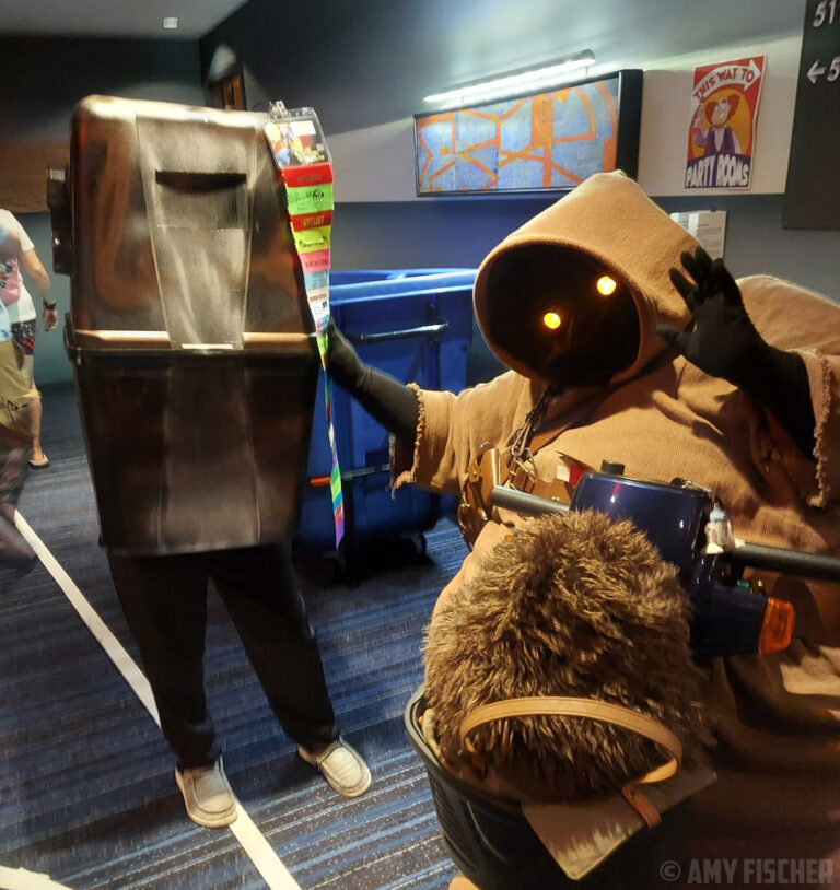 A jawa on a mobility scooter gestures towards a gonk in the parties hallway at CONvergence